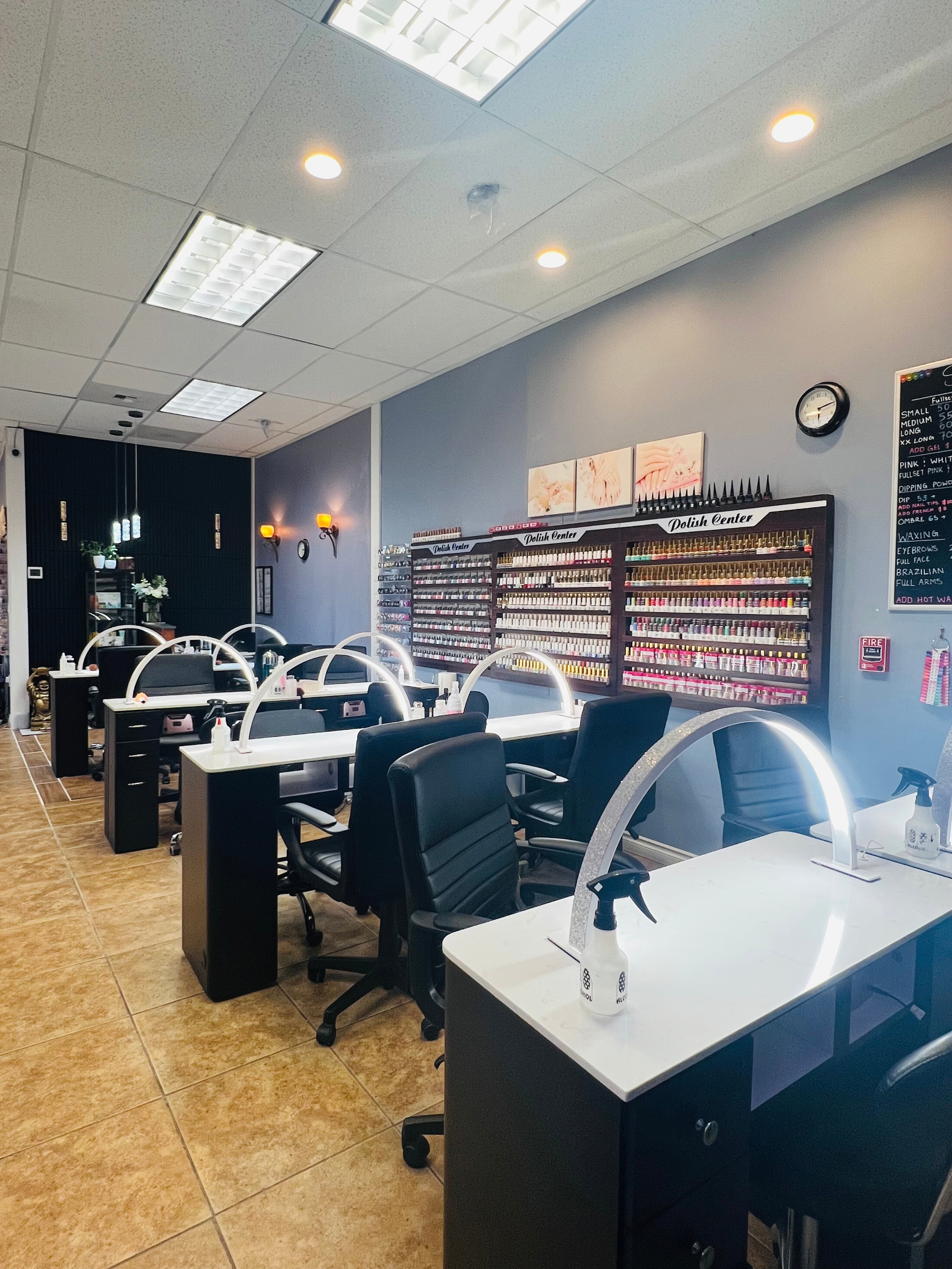 Four nail salon tables with lighting. There is a polish center on the wall with a variety of polish colors displayed