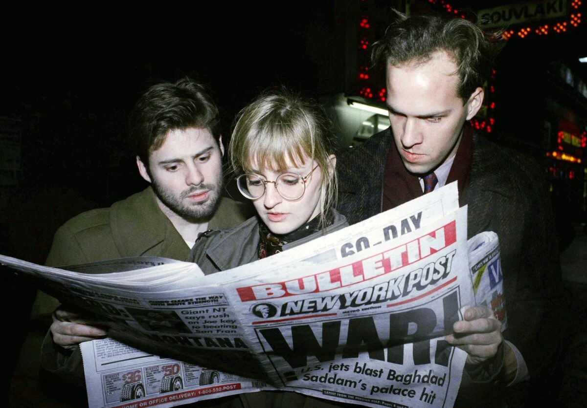 Rebecca Spice, a tourist from Milwaukee, Wisconsin, is flanked by Joel Kopischke, left, and Robert Simonson, both of New York, as they read a bulletin edition of the New York Post reporting the outbreak of hostilities in the Persian Gulf in New York…