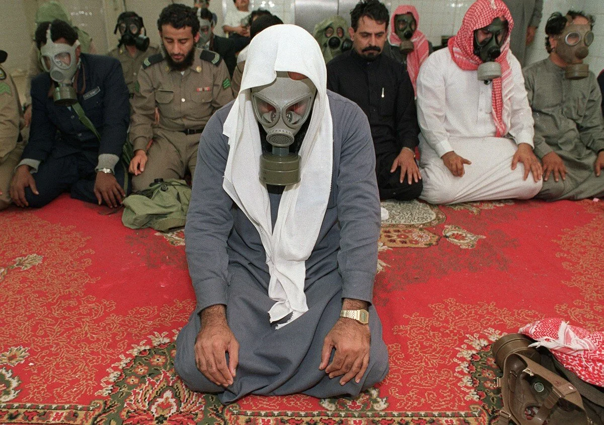 Soldiers, hotel workers and others, some wearing gas masks, kneel for morning prayers on January 18, 1991, in a basement used as a bomb shelter at a hotel in eastern Saudi Arabia. A Scud missile fired by Iraq had reportedly been intercepted and dest…