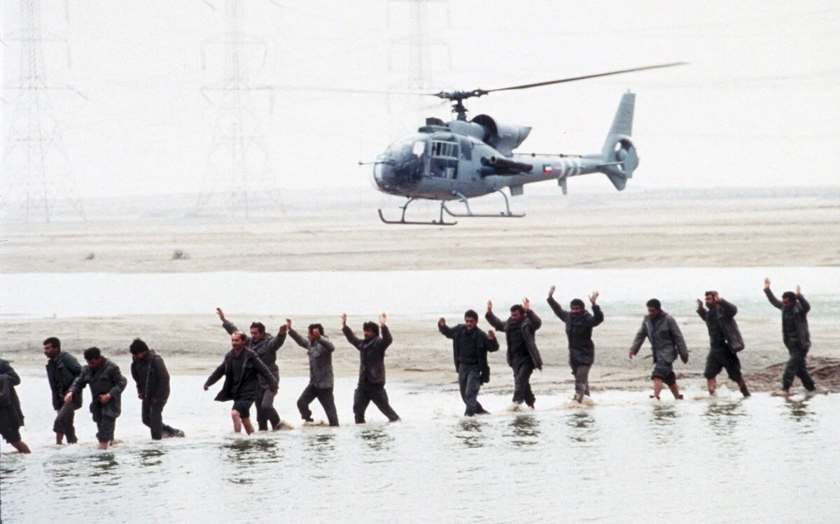 A Kuwaiti helicopter herds Iraqi prisoners of war, arms in the air, across a stream in southeastern Kuwait, on February 25, 1991. AP