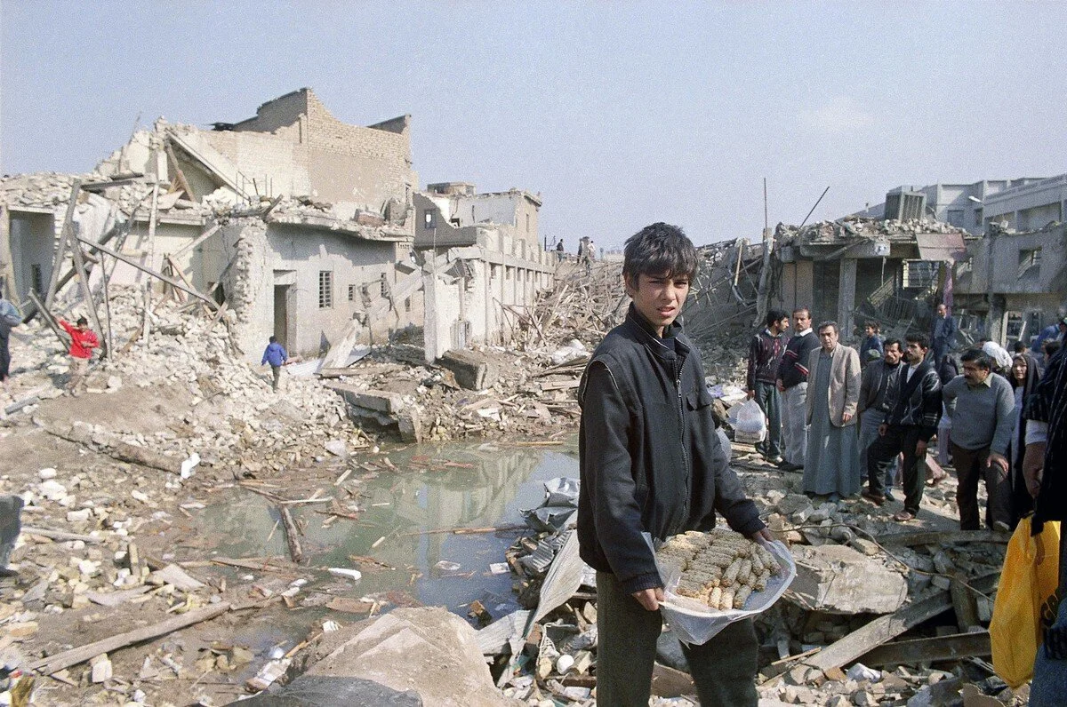 A young Iraqi boy carried a plate of sausage in the ruins of houses in an area west of Al-Ahrar Bridge, Baghdad, on February 20, 1991, after a recent allied bombing raid. John Rice / AP