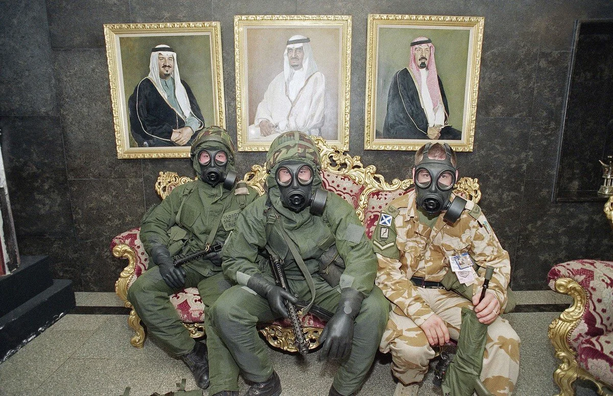 Three British soldiers in full combat and gas gear wait for the all-clear signal in a hotel lobby in Dhahran, Saudi Arabia, during a Scud attack on February 26, 1991. The three wait under the portraits of the present and former Saudi monarchs. J. Sc…