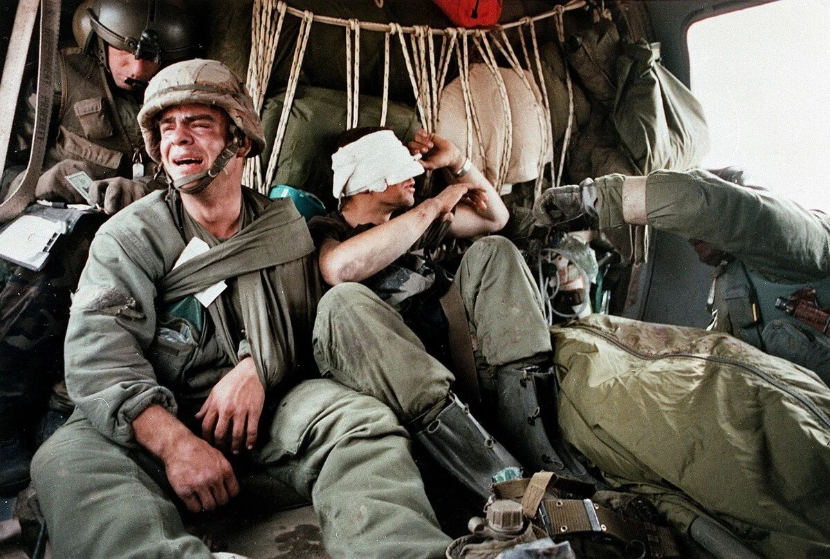 A wounded Ken Kozakiewicz, left, cries after being given the dogtags and learning of the death of a fellow tank crewman, in the bodybag at right, in this February 28, 1991 photo. The widely published photo came to define the Persian Gulf war for man…