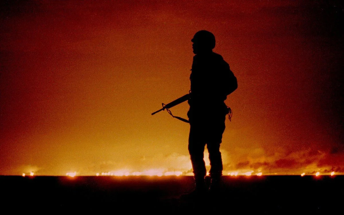 A U.S. soldier stands night guard as oil wells burn in the distance in Kuwait, just south of the Iraqi border on February 26, 1991. Andy Clark / Reuters
