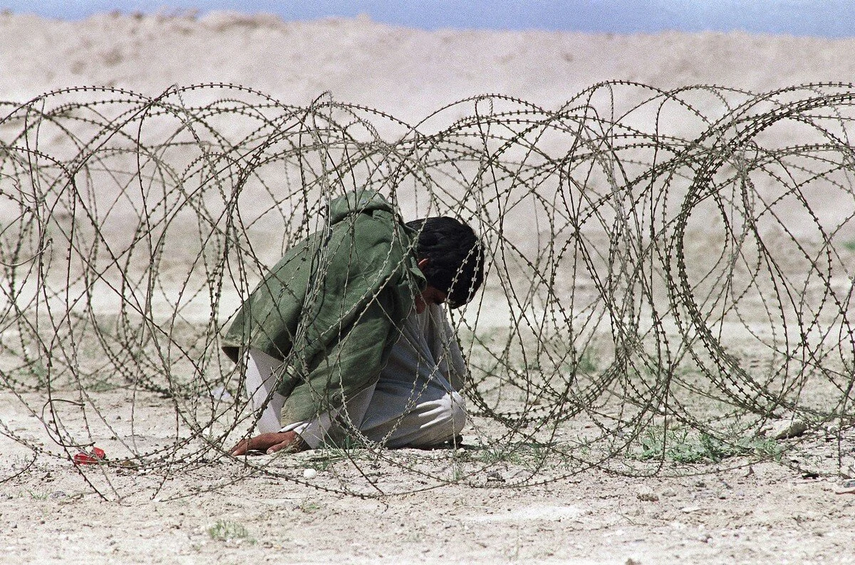 An Iraqi sits huddled in a barbed wire holding area at a U.S. checkpoint some 25 miles south of Basra, on March 28, 1991 in Iraq, after he and four others were arrested by U.S. soldiers for allegedly robbing and murdering refugees. Four members of t…