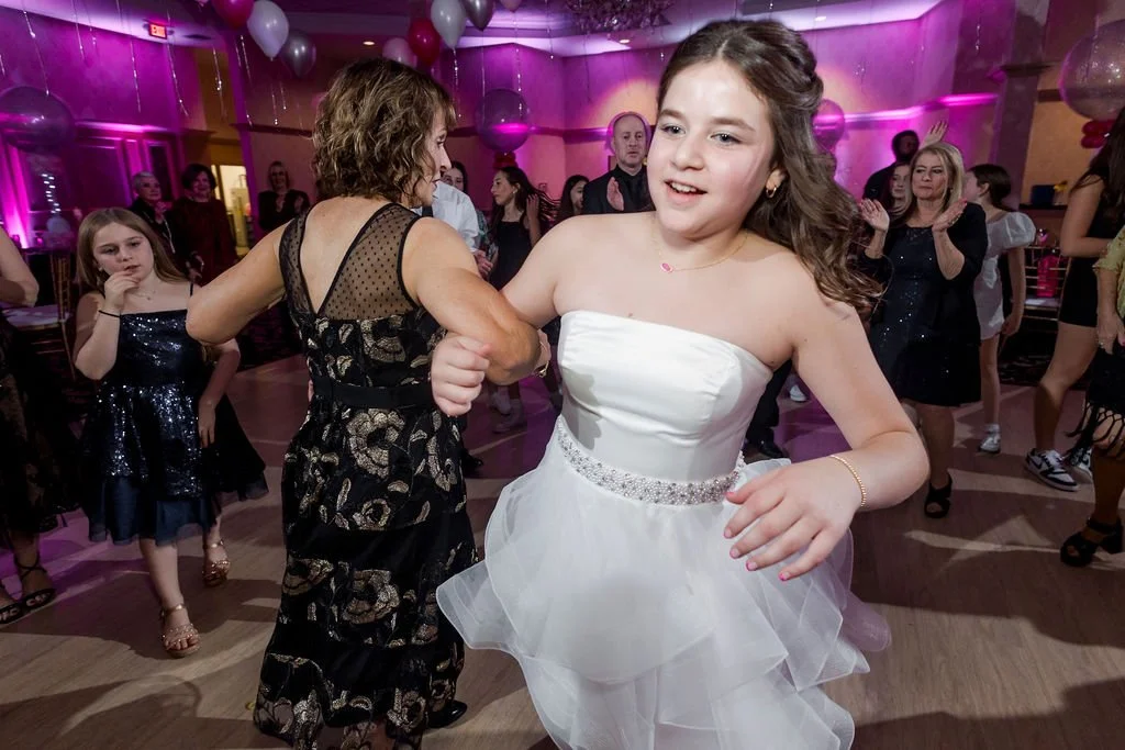 Young girl in a white dress dancing at a party with other people in the background.