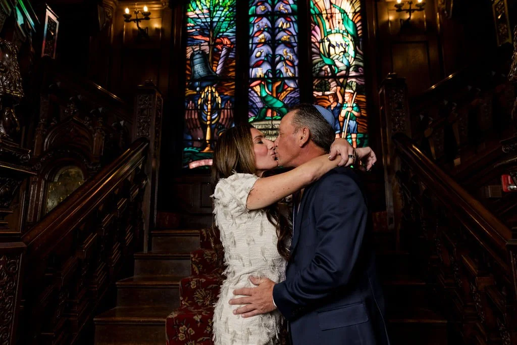 A couple kissing inside a church with stained glass windows in the background.