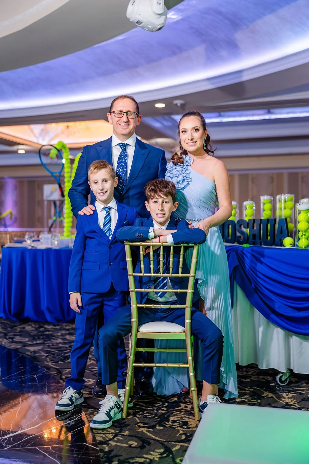 A family of four dressed in blue at a celebration, with a decorated table in the background.