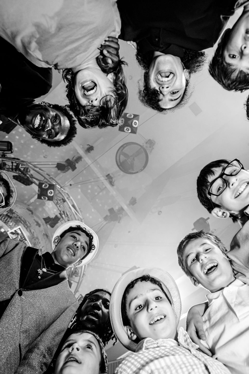 Group of diverse children and teens smiling and looking down at the camera in a circle at a party or celebration.