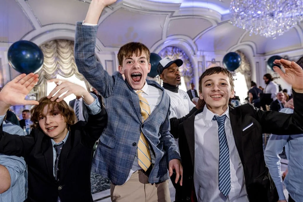 Three boys celebrating at a formal event in a decorated ballroom with chandeliers and balloons.
