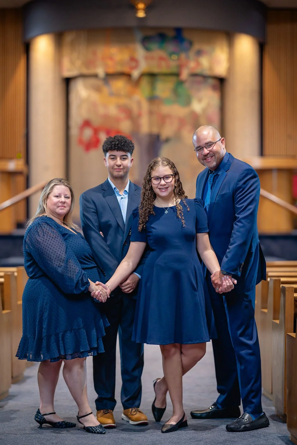 A family of five standing together inside a church, dressed in blue attire, with a blurred religious artwork in the background.