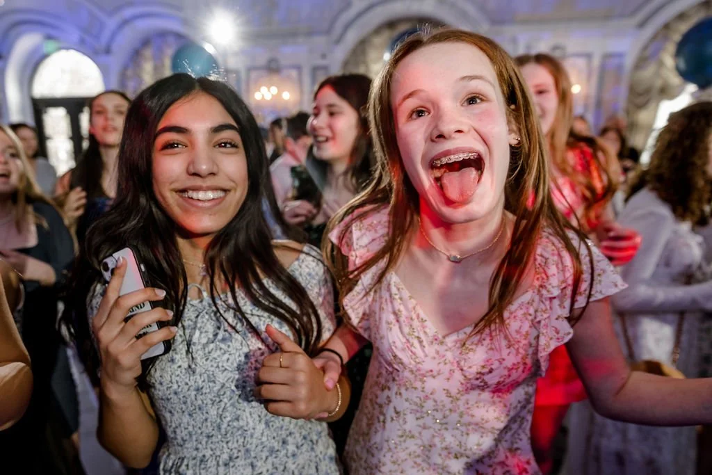 Two young girls smiling and having fun at a lively indoor party or celebration.