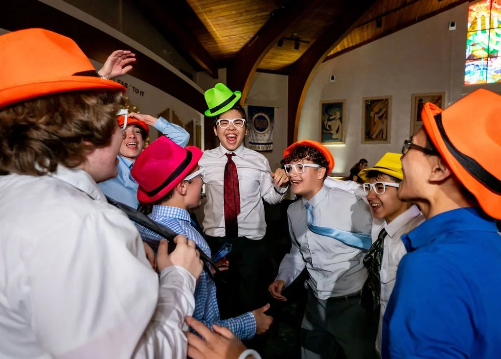 Group of children in a church or community hall wearing colorful hats, laughing and smiling.