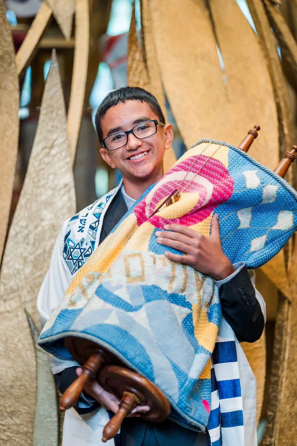 Young boy smiling and holding a Torah scroll during a Jewish celebration or ceremony.