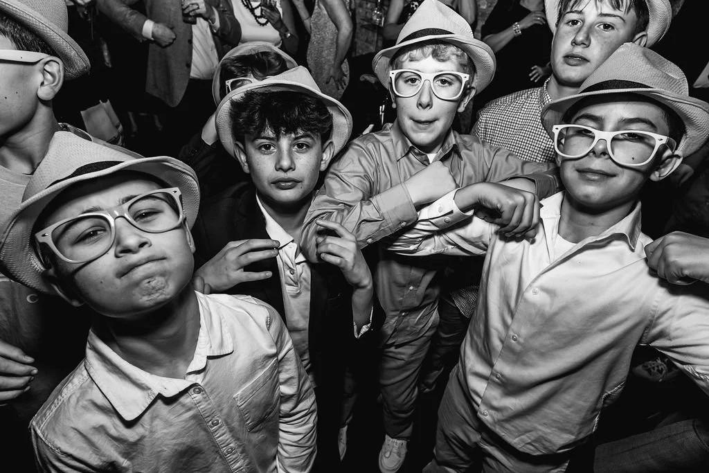 Group of boys wearing hats and large glasses at a party or event, posing in front of a crowd.