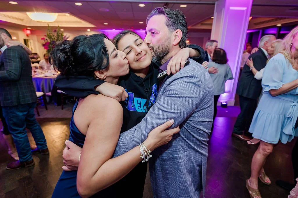Three people hugging and being affectionate at a lively social event with purple lighting.