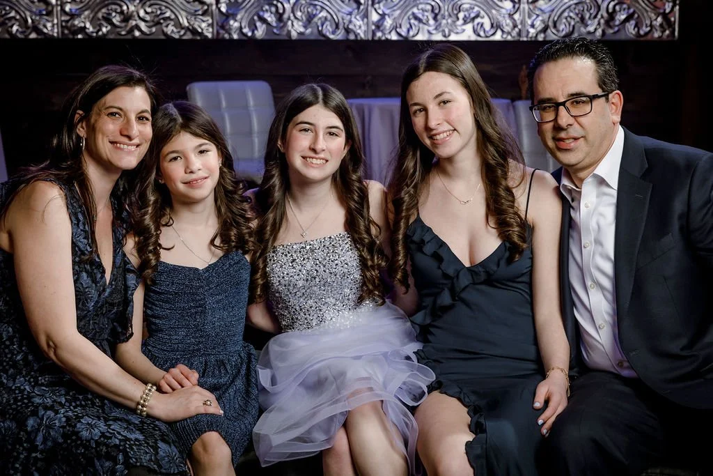 A family of five sitting together in formal attire, at an indoor event, smiling for the camera.