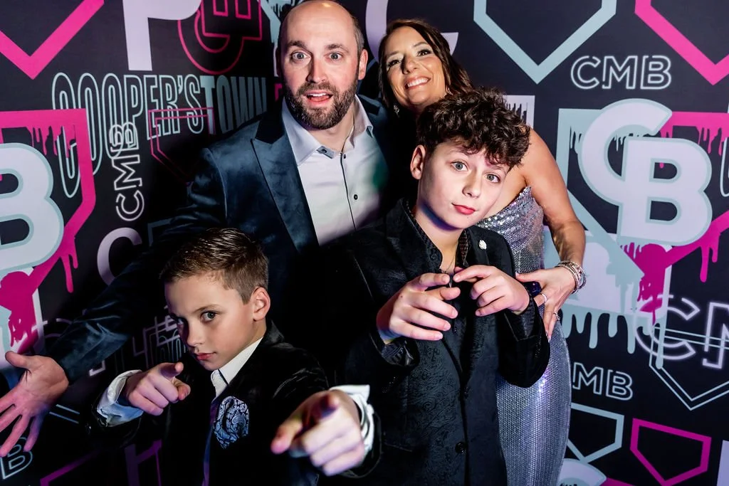 Four people, two adults and two boys, posing in front of a colorful graffiti wall at an event. The man and woman are smiling, while the boys strike confident poses.