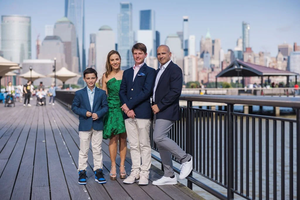 A family of four standing on a pier with the New York City skyline in the background.