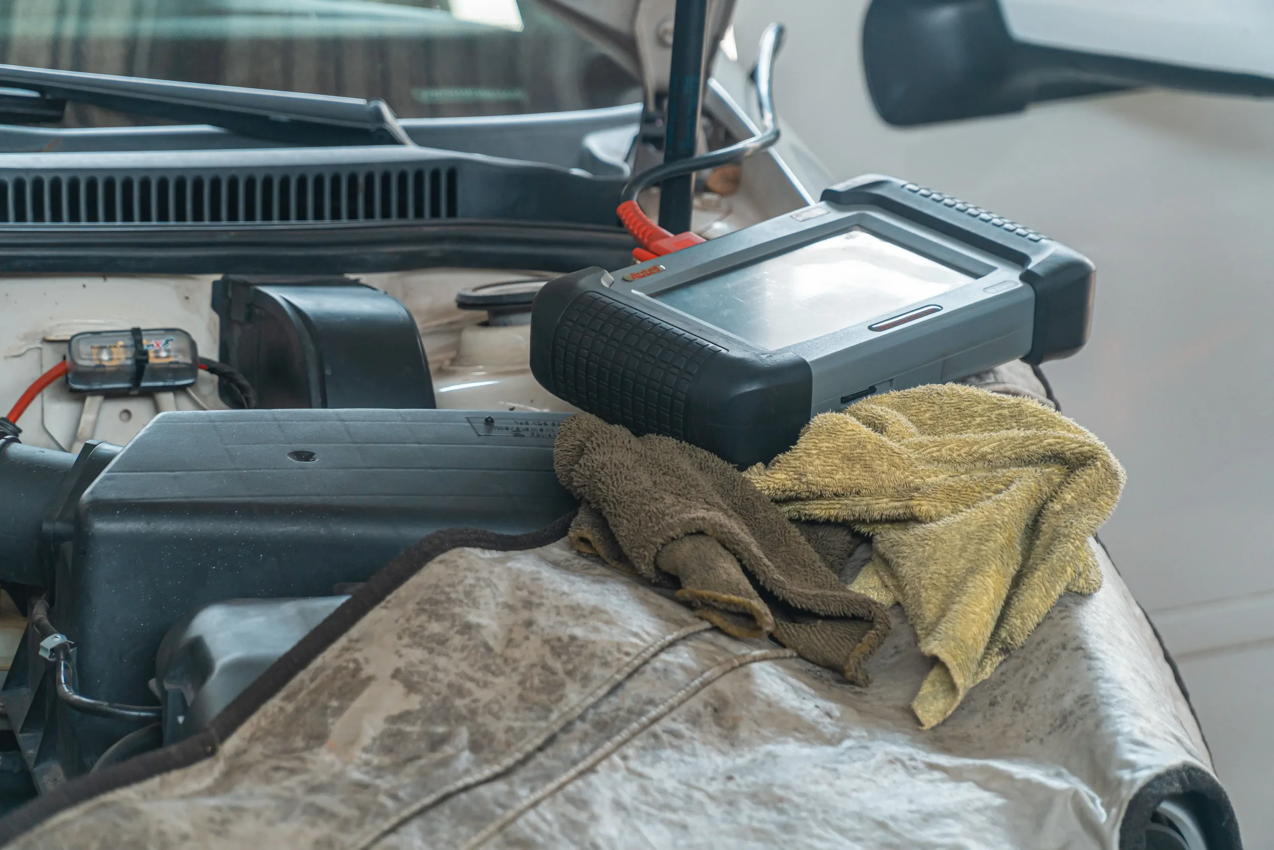 An OBD-II scan tool lays on the engine bay of a car as a technician gets ready to ready trouble code's from the vehicle's engine computer.