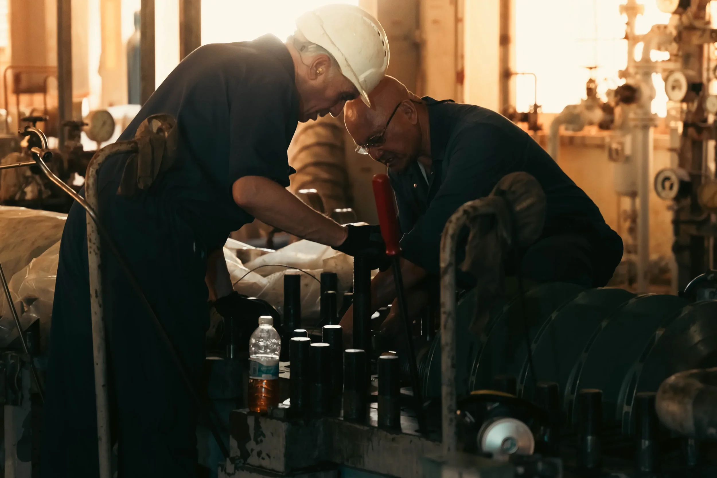 Two Men Carefully Work on a Machine to Prevent Overgreasing the Bearings Inside of It.