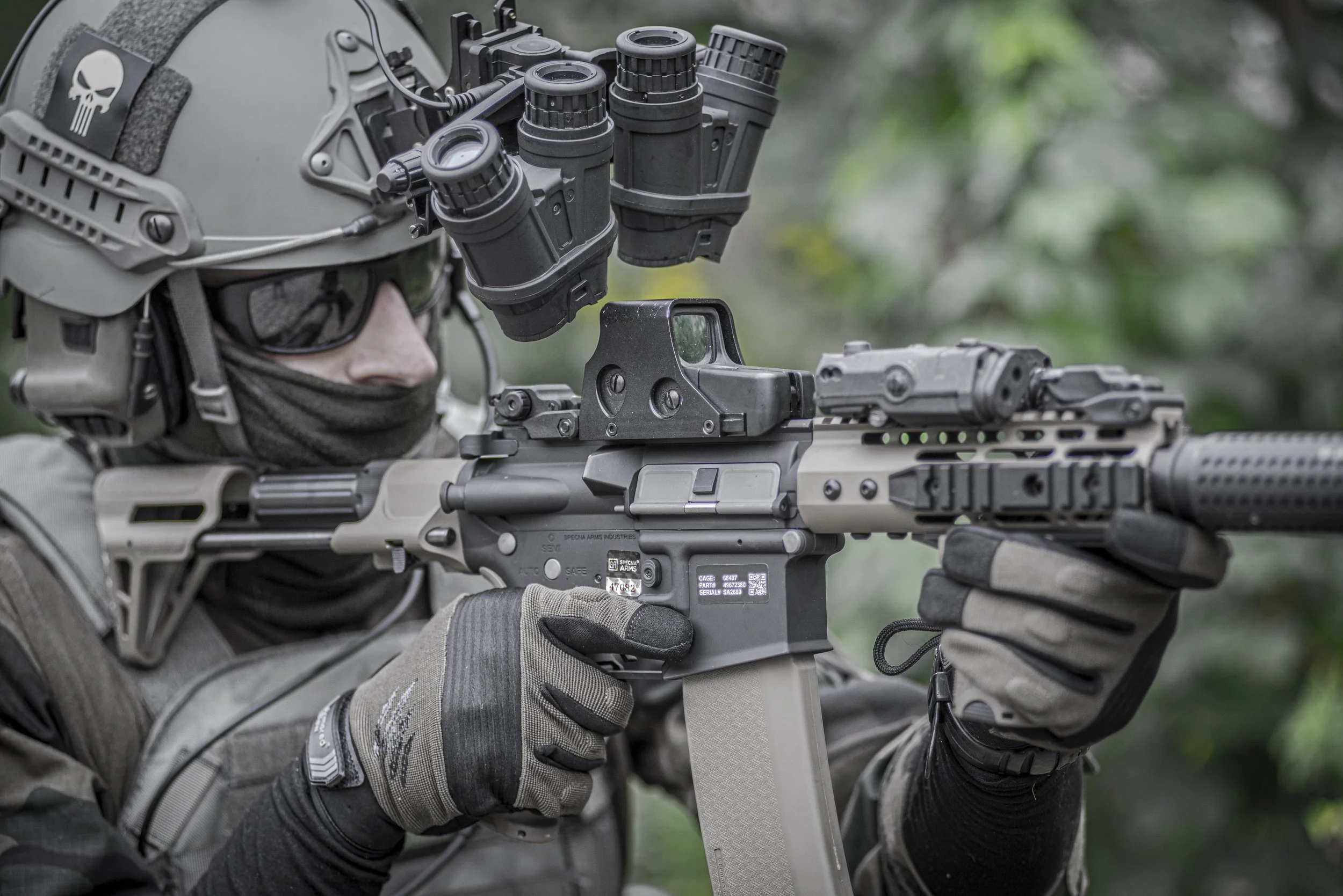 Tactical shooter aiming a short AR-platform carbine equipped with holographic sight, laser unit, and night-vision gear.