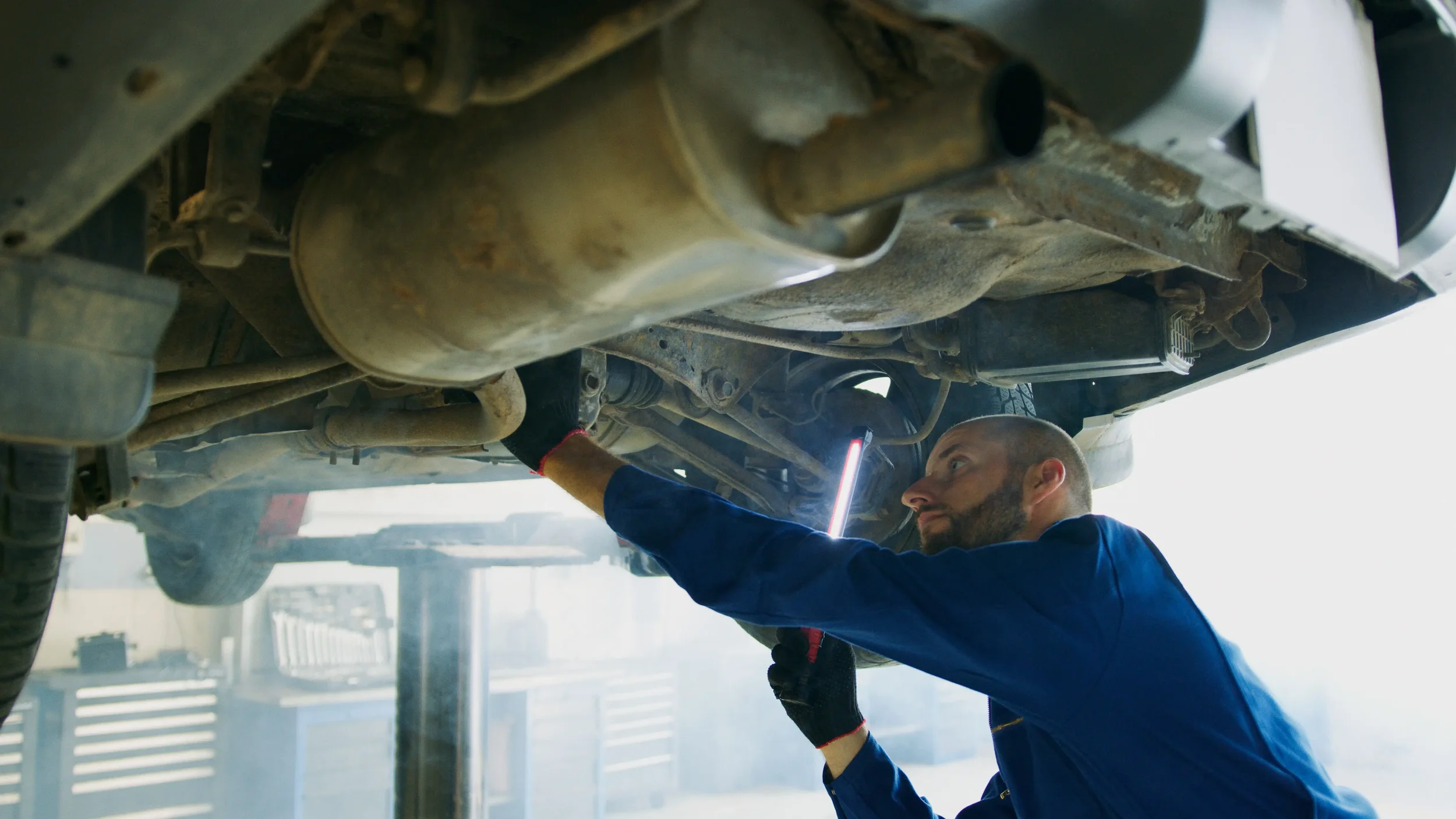 A mechanic inspects an automotive catalytic converter installed in an exhaust system to reduce harmful vehicle emissions.