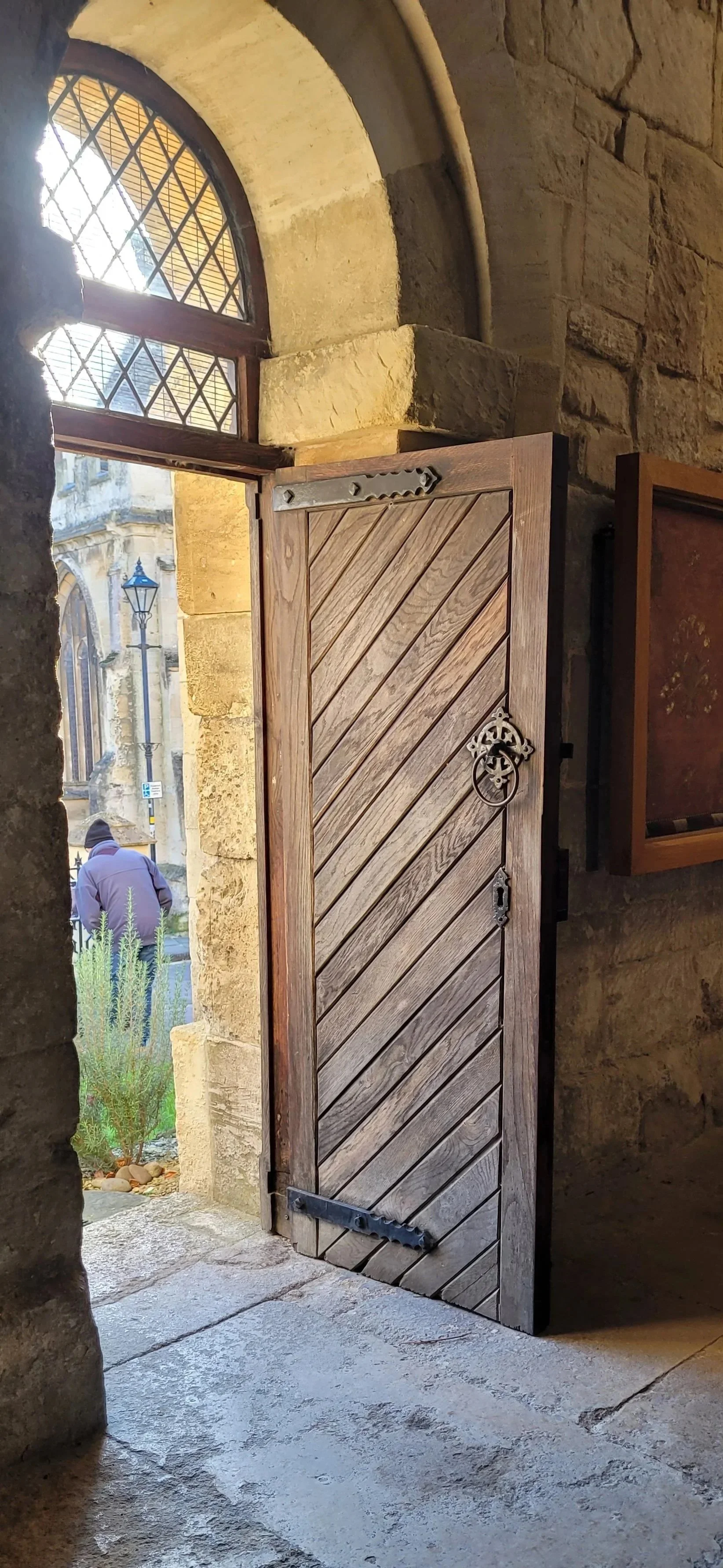 Kerryn Powell regularly uses a door as a metaphor for unlocking conversations. Her is an open wooden door with metal hinges and handle, to a stone church or historic building with arched window and street scene beyond