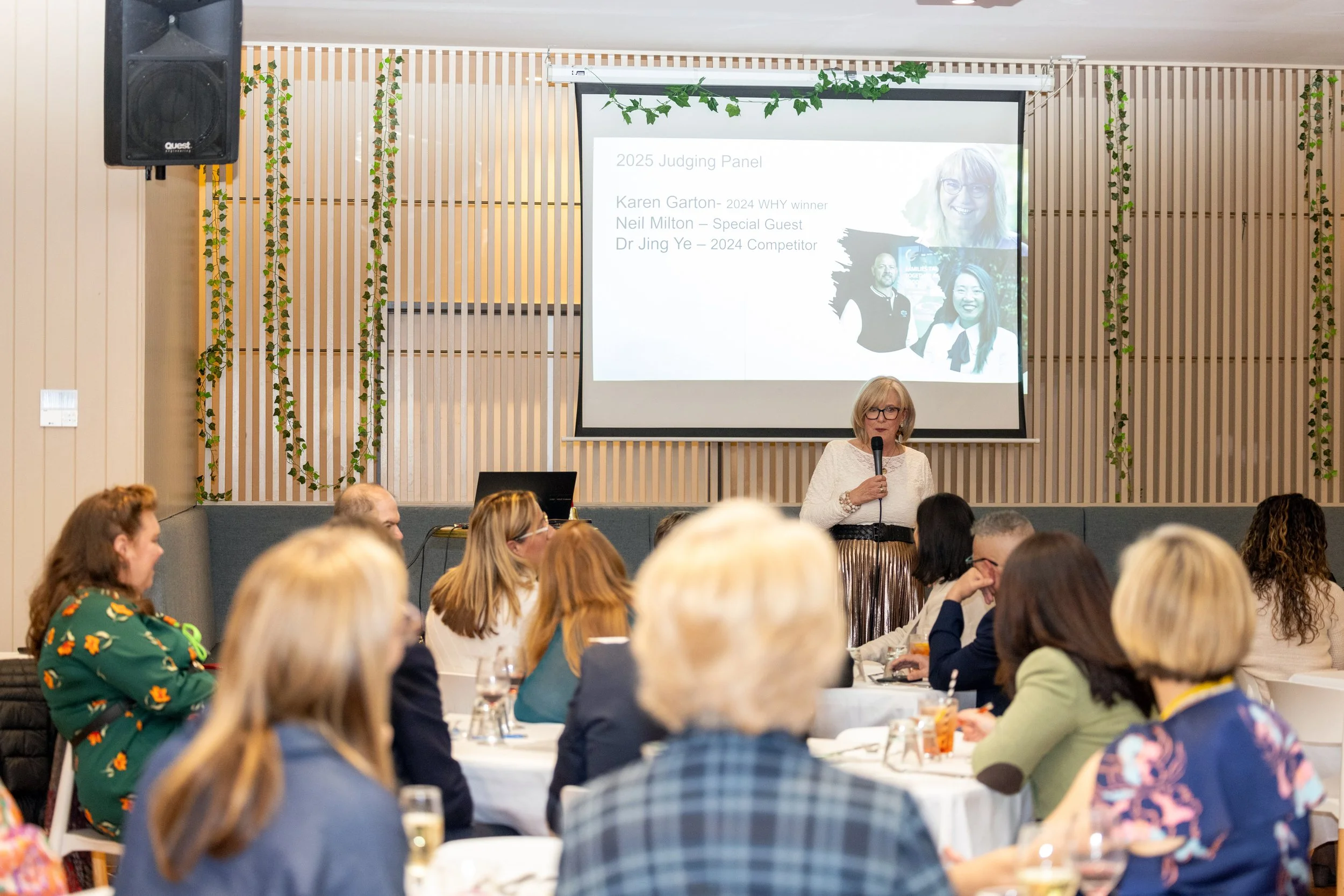 Kerryn  Powell is facilitating an event for the Your Time MAtters business networking community she established in Melbourne, Victoria Australia. She is standing in front of a room of seated people, holding a microphone and speaking.