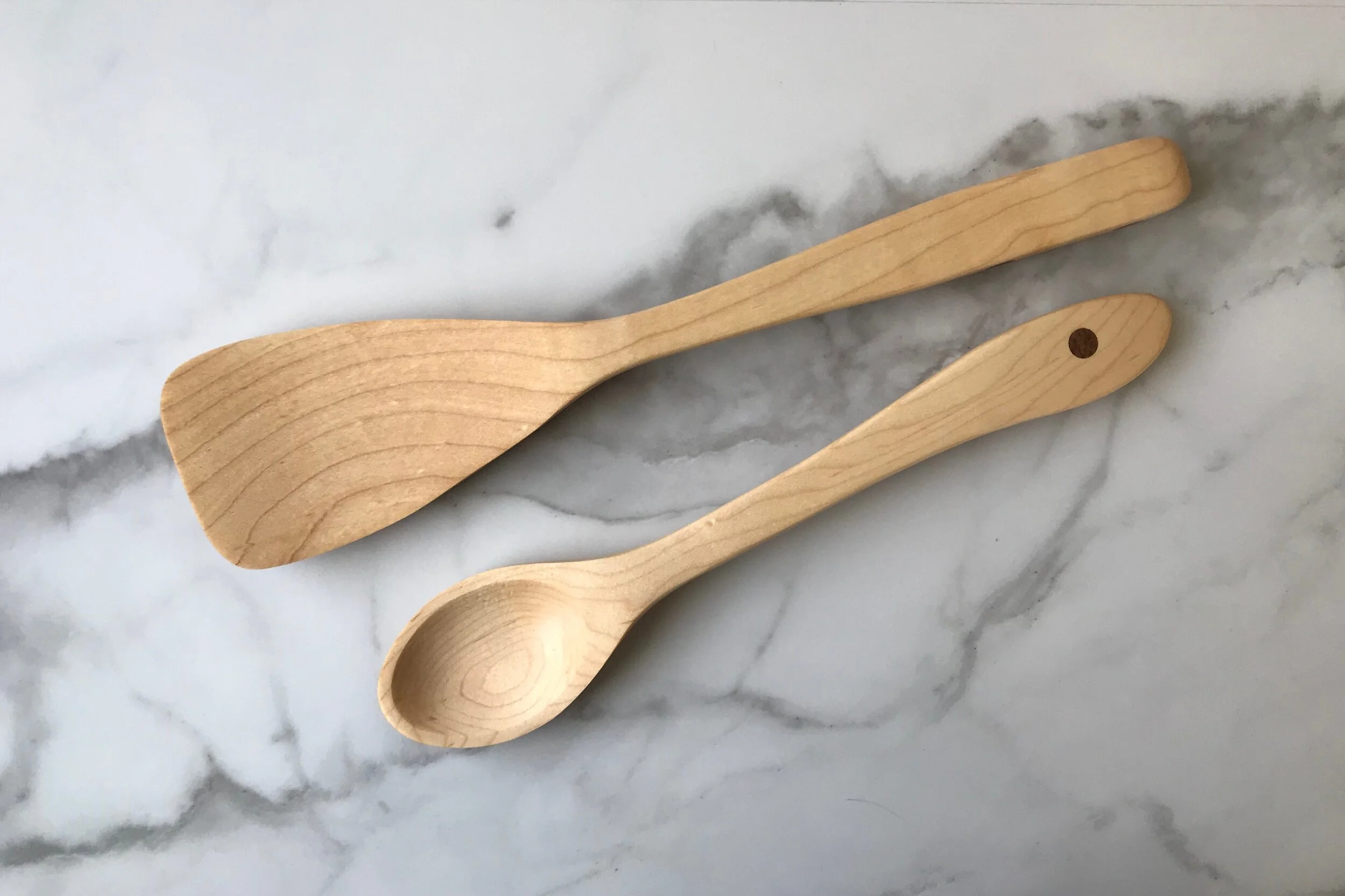 Two wooden kitchen utensils, a spatula and a spoon, placed on a white and gray marble surface.