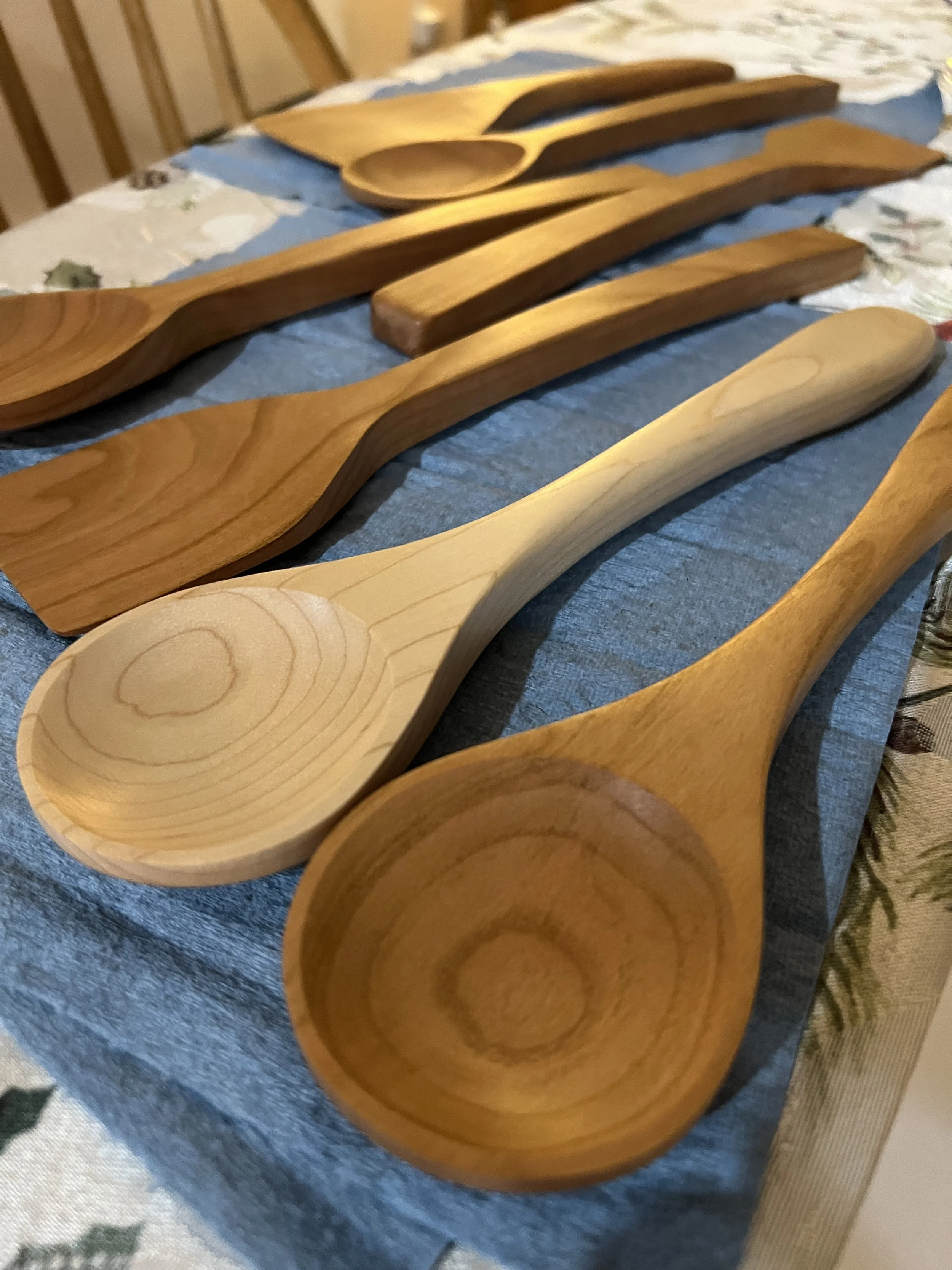 A collection of wooden spoons and spatulas on a blue cloth, arranged in a row for display.