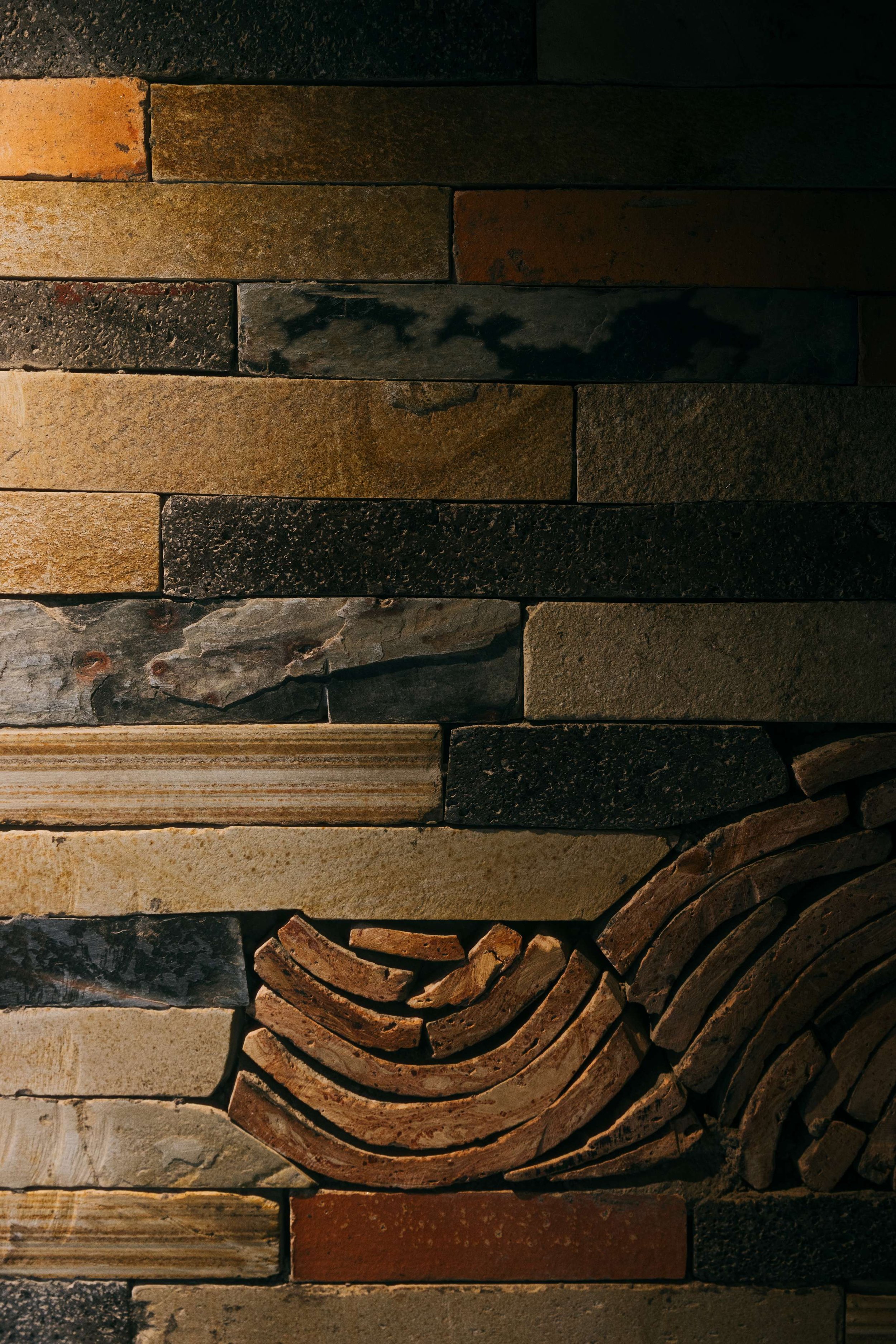 Detail of Bisate Sanctuary's layered stone and brick wall featuring an inset curved mosaic pattern, showcasing the artisan craftsmanship and mixed local materials used throughout the spa — Black Sable