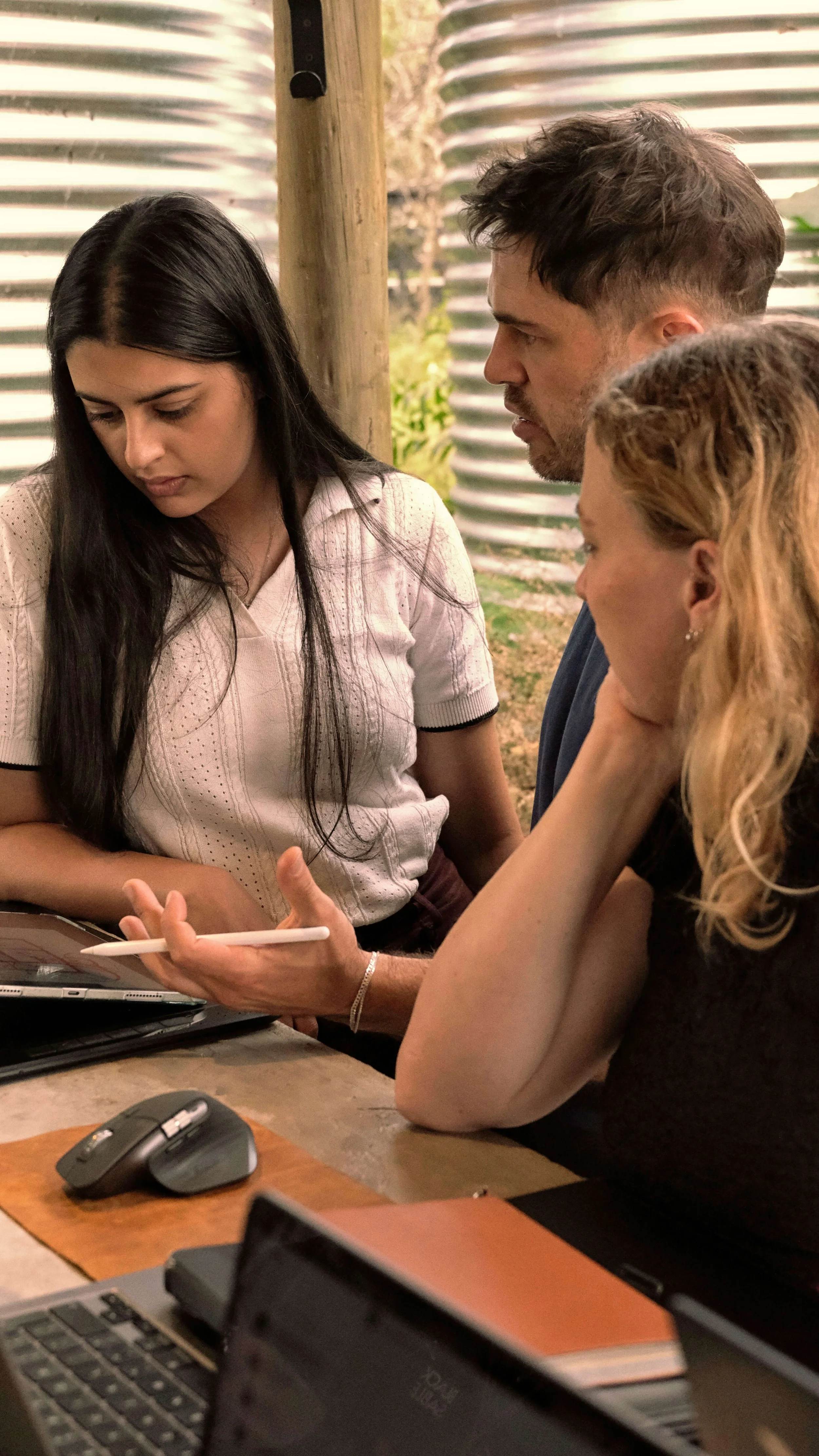 Three Black Sable team members gathered closely around a tablet, reviewing digital design work together in a covered outdoor workspace.