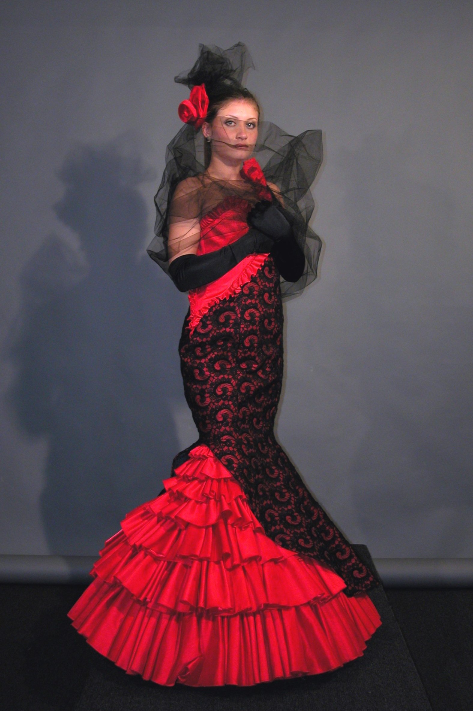 Model wearing Flamenco inspired floor length black and red gown, paired with a headpiece and gloves. 