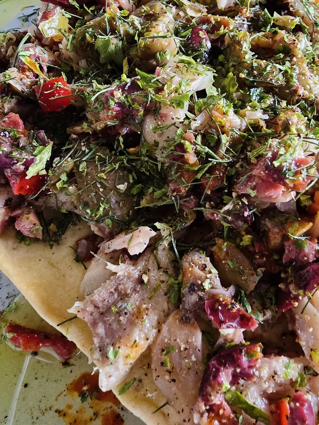 Close up of sardines and muffuletta olive mix on a sesame cracker, topped with dried herbs and olive oil