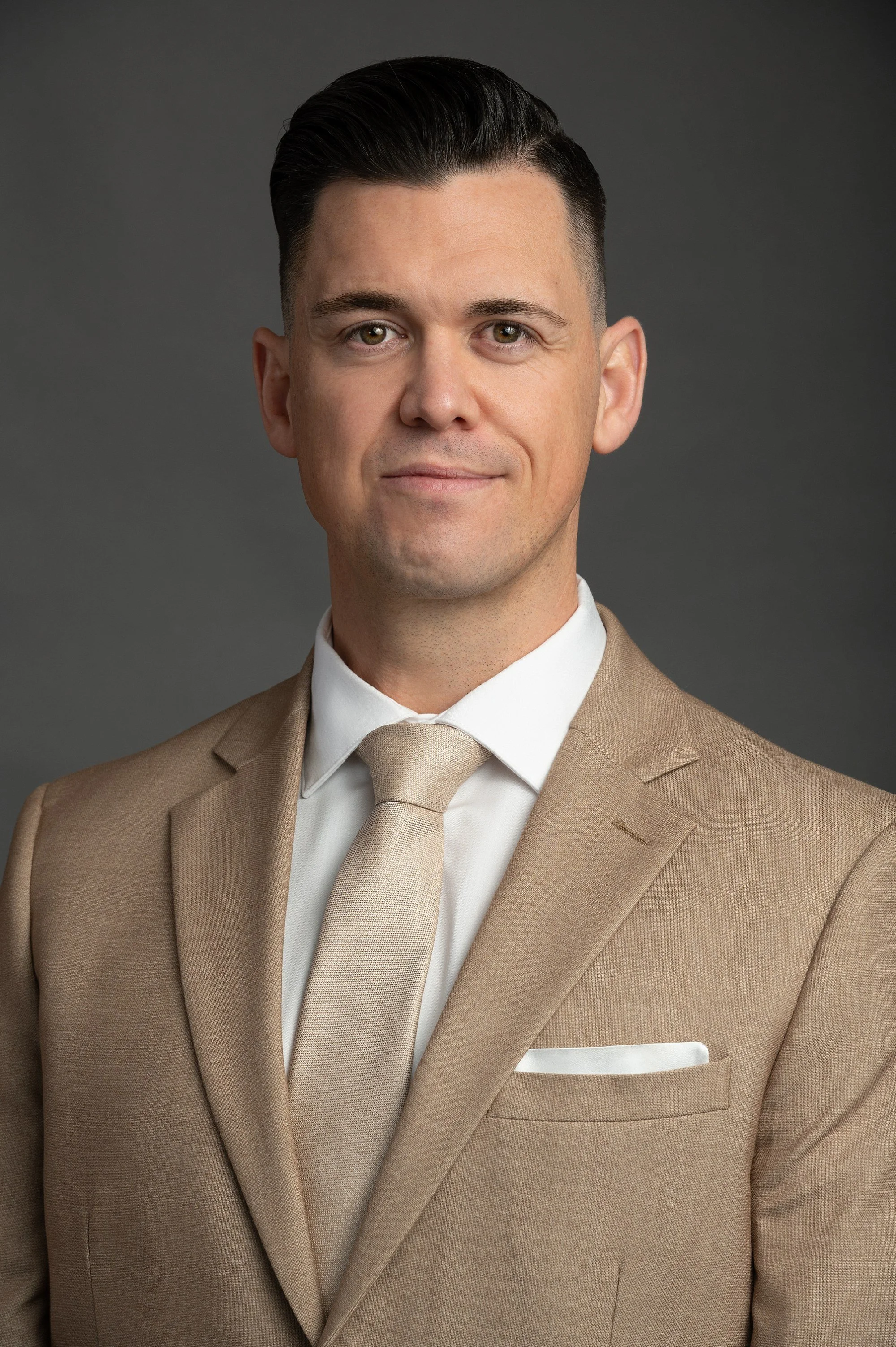 Man in tan suit with white shirt and tie on gray background.