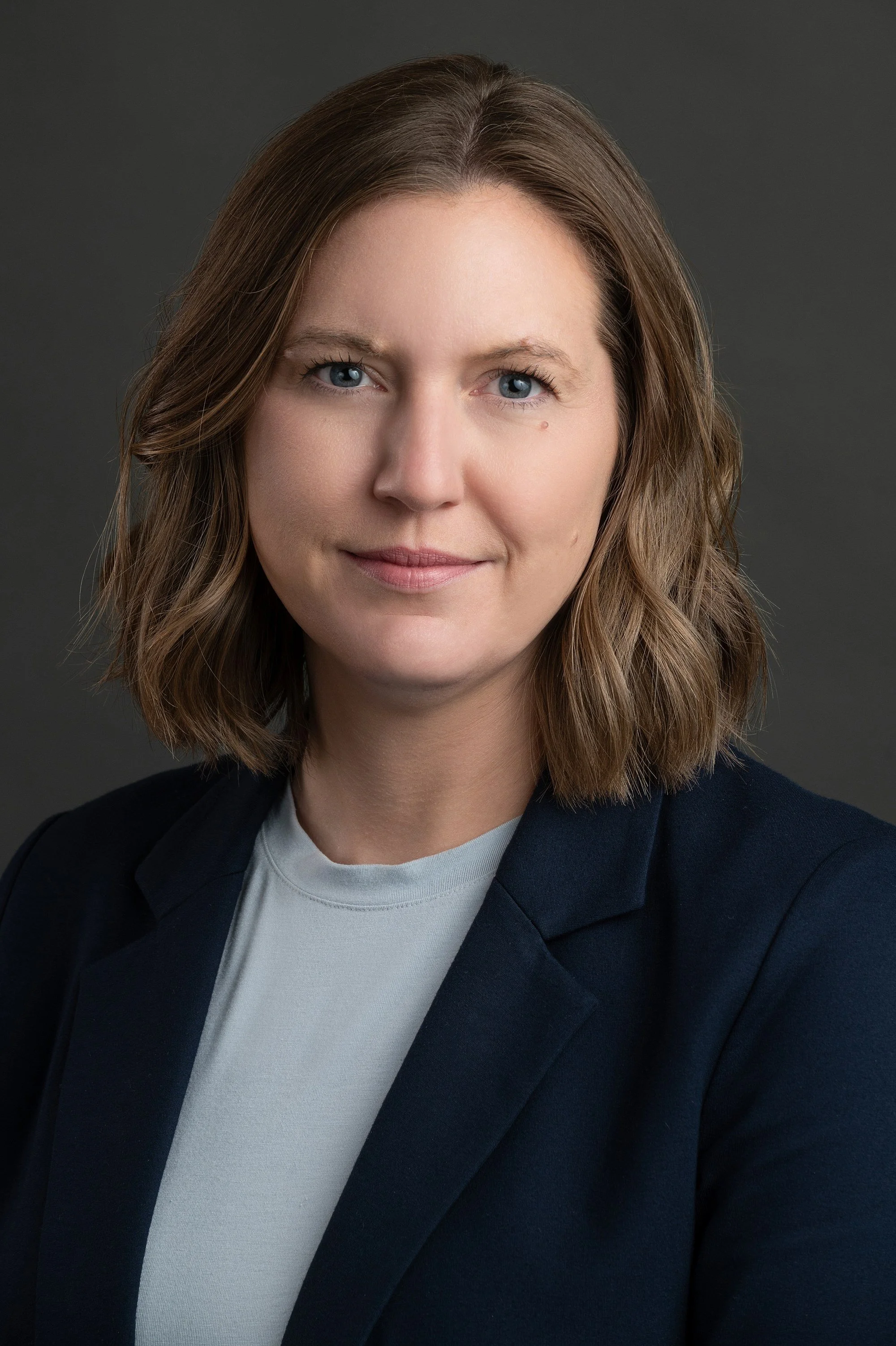 Portrait of a woman with shoulder-length brown hair, wearing a dark blazer and a light shirt.
