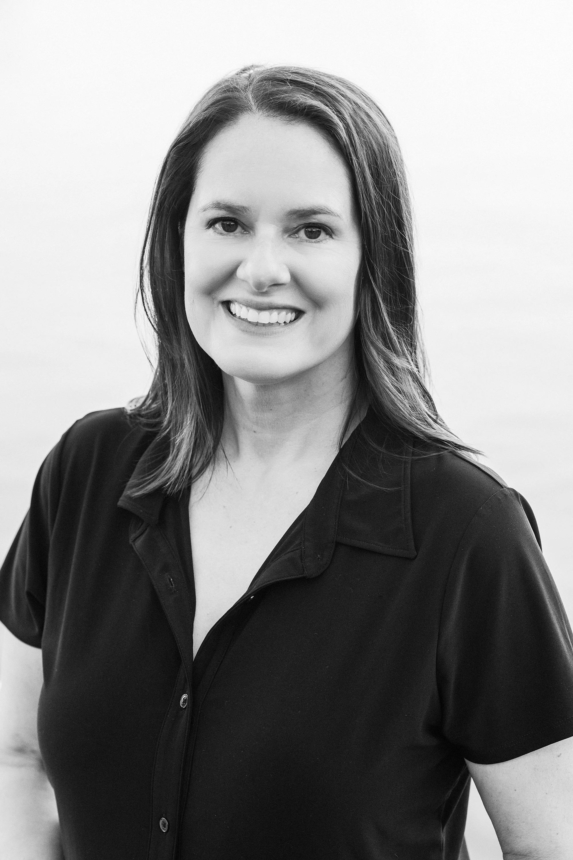 A woman with shoulder-length hair smiling, wearing a dark button-up shirt, in black and white.