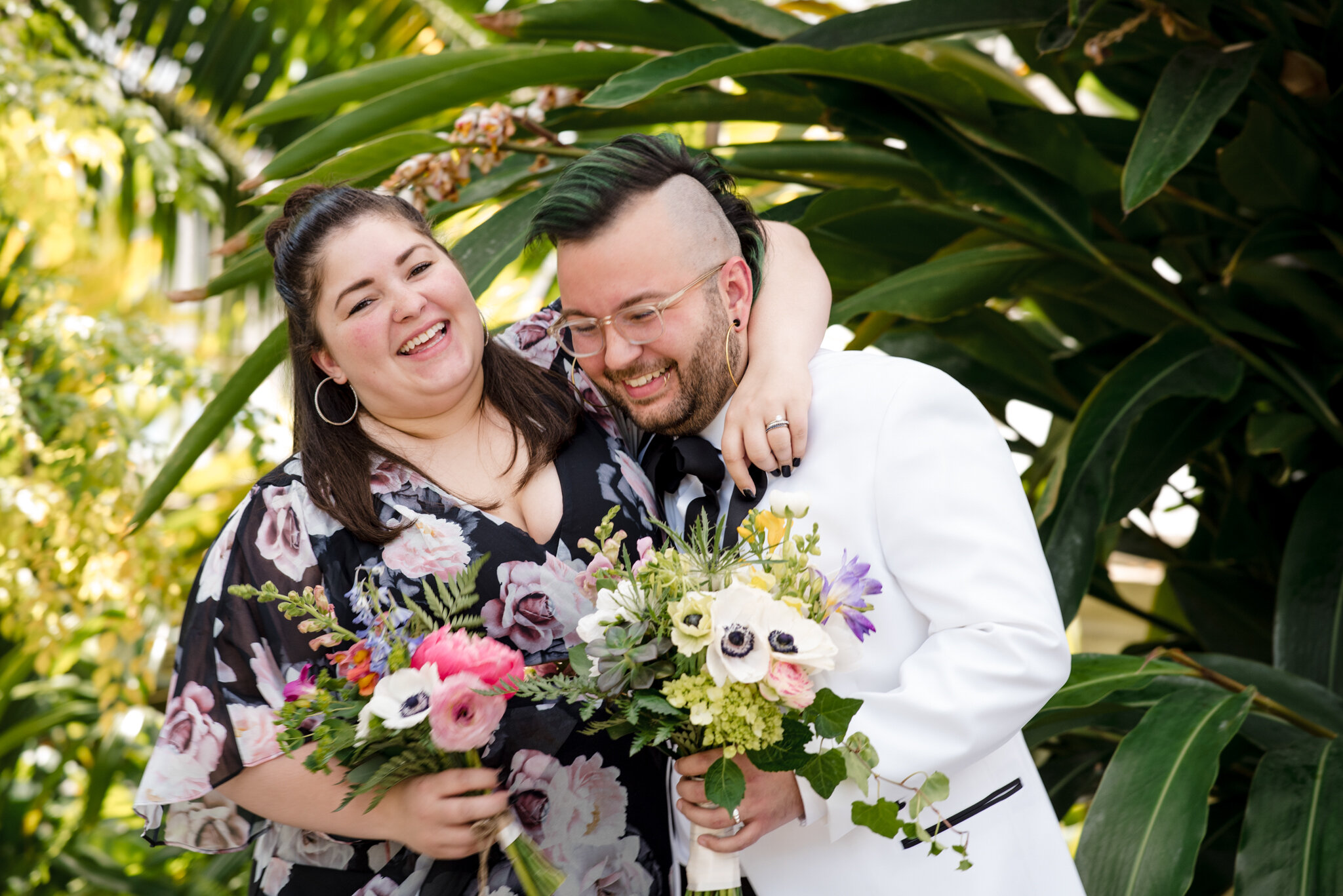 Marrier in white suit and guest in dress hug with bouquets before ceremony at Roger Williams Botanical Center Providence Rhode Island Michelle Schapiro New England Portrait Photographer