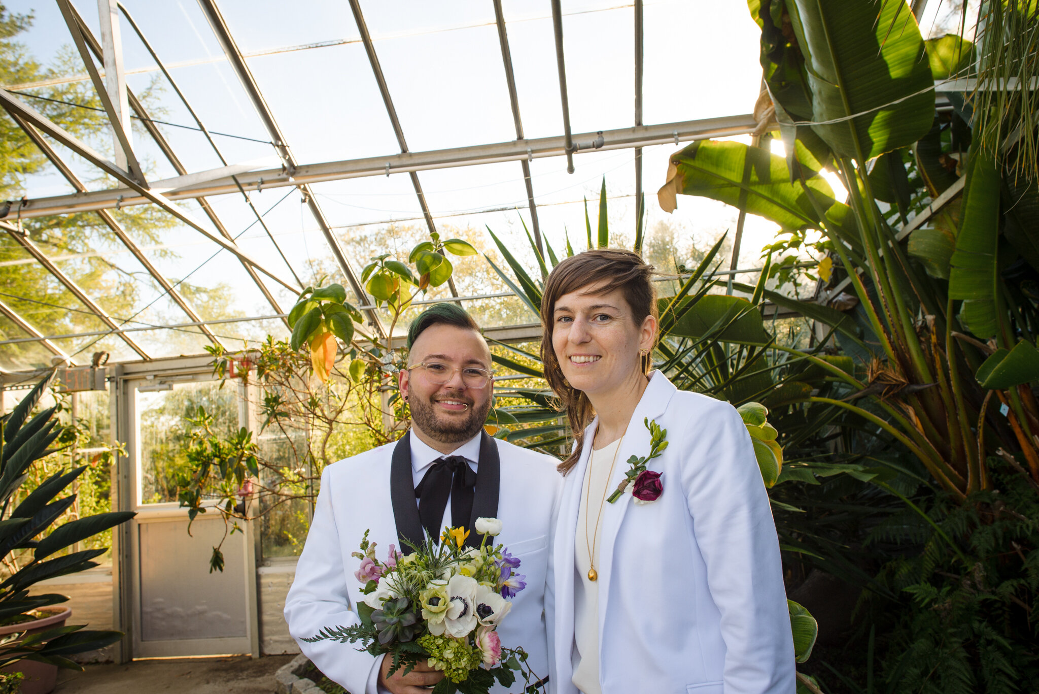 Marriers in white suits smile in greenhouse at Roger Williams Botanical Center Providence Rhode Island Michelle Schapiro New England Couple Photographer