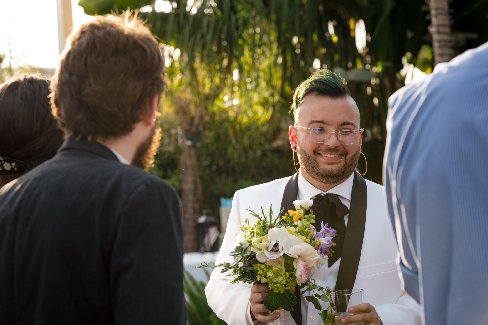 Marrier in white suit holds bouquet and greets guests during reception at Roger Williams Botanical Center Providence Rhode Island Michelle Schapiro New England LGBTQ Photographer