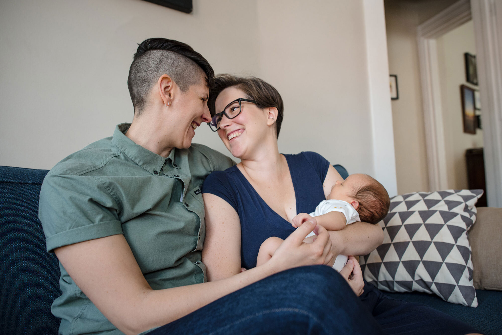 New parents cradle infant together on couch during at home Boston newborn session Michelle Schapiro LGBTQ Family Photographer