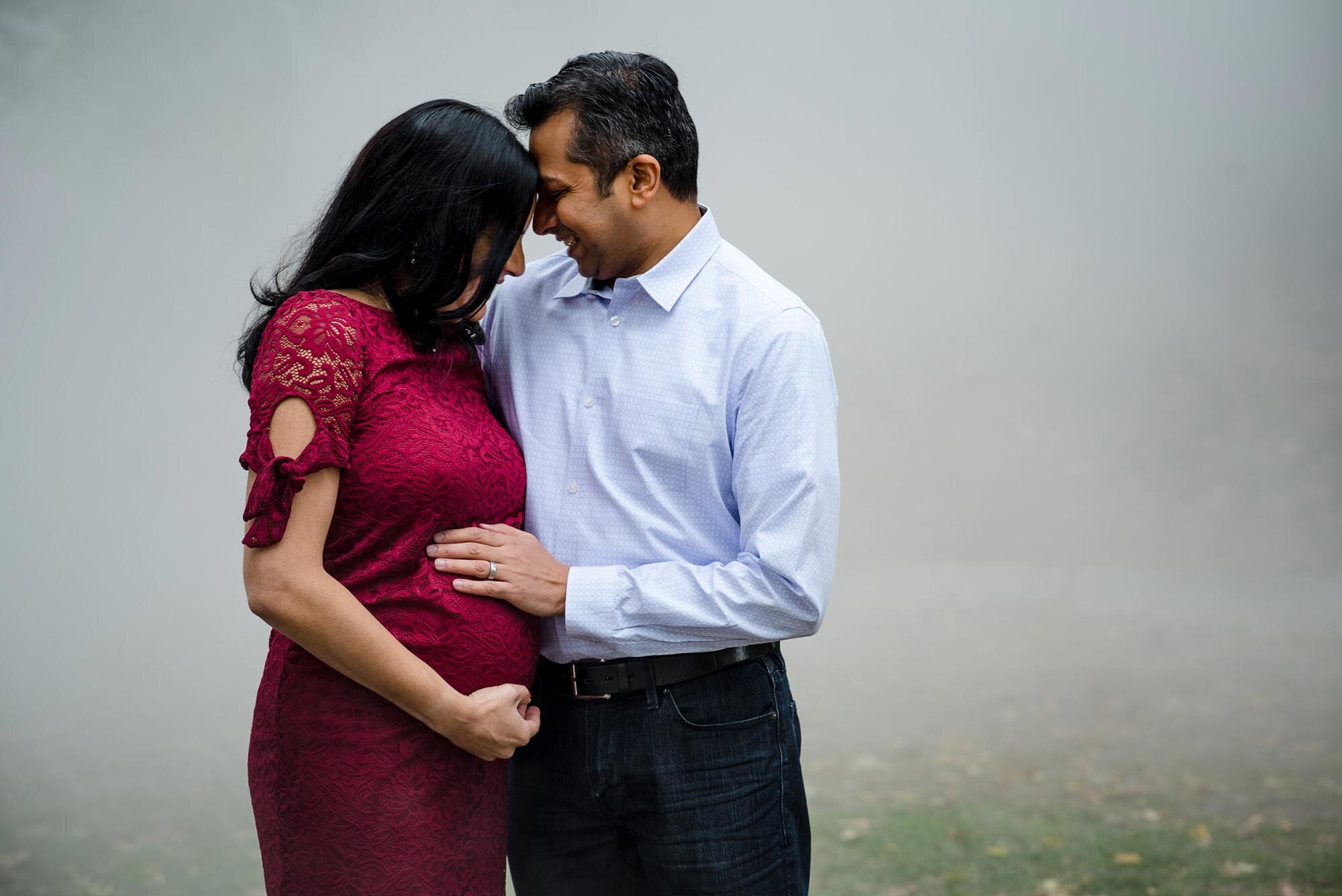 Expectant parents cradle belly and embrace with fog rolling in behind them during autumn pregnancy photo session Michelle Schapiro Family Photography