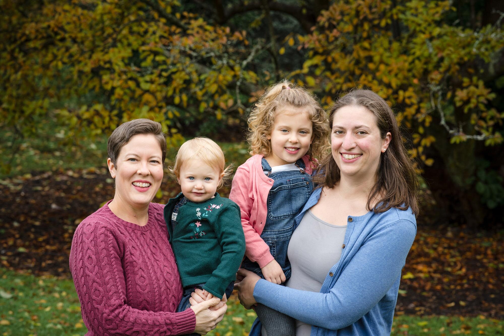 Parents hold two young children during autumn family photo session in Boston park Michelle Schapiro Photography