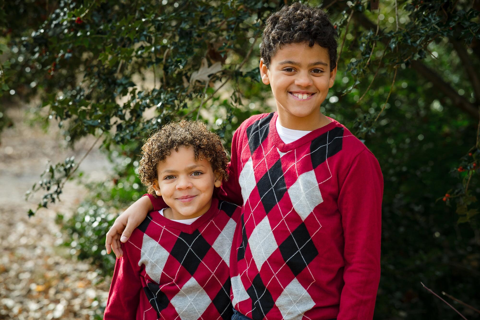 Two young siblings in matching red sweaters hug during family photo session in Boston park Michelle Schapiro Photography