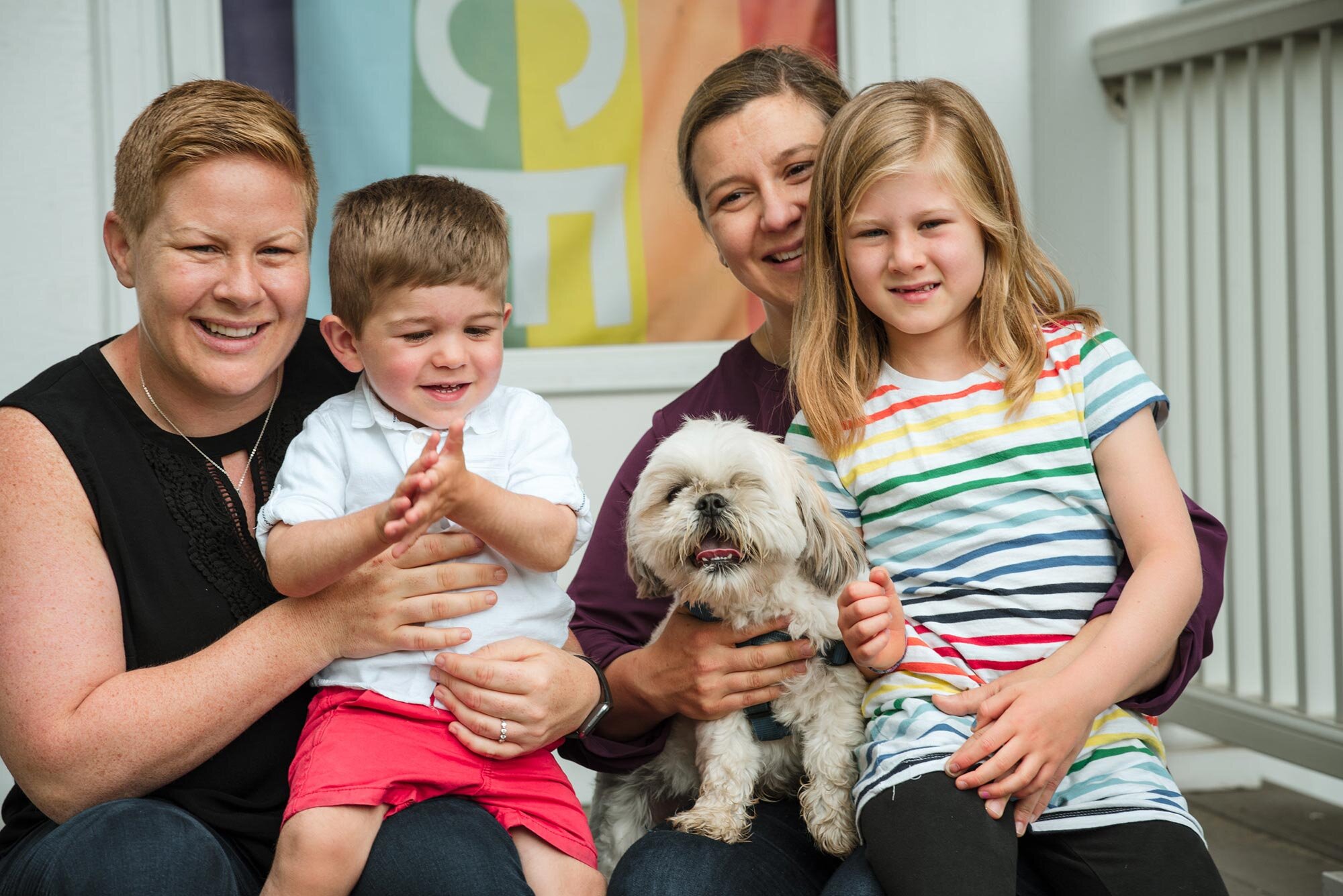 Parents and two young children and dog sit together on front porch of home during LGBTQIA family session Michelle Schapiro Photography