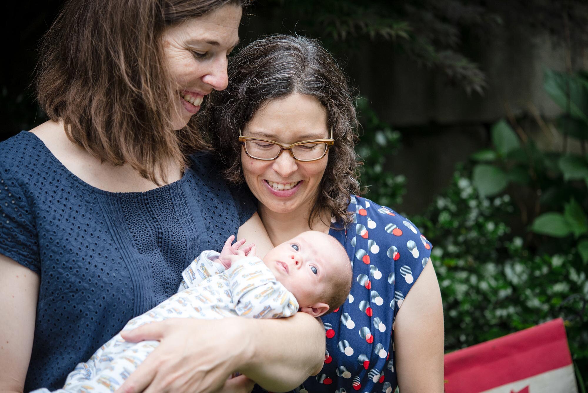 Parents cradle newborn baby in arms in Boston park during family photo session Michelle Schapiro New England LGBTQ Photographer