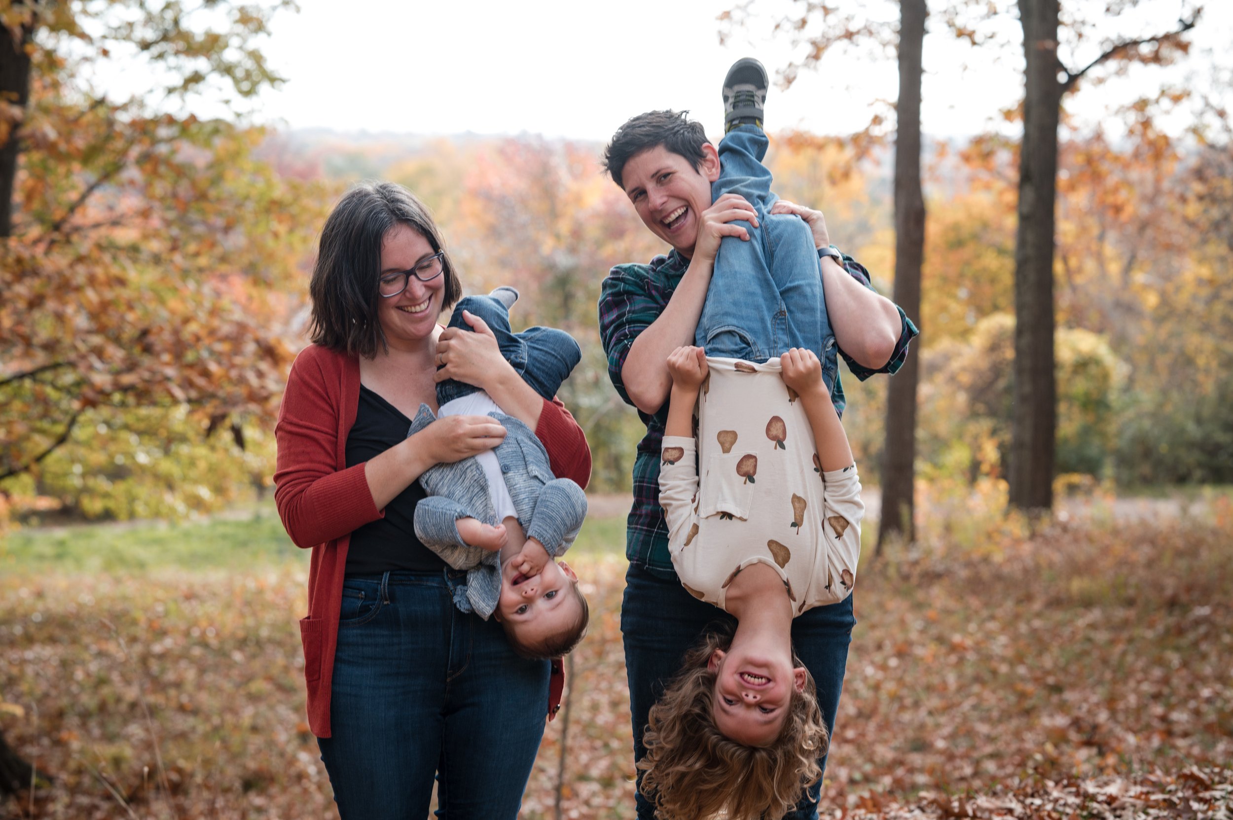 queer parents hold toddlers upside down in candid playful family photos in fall foliage by Michelle Schapiro Photography