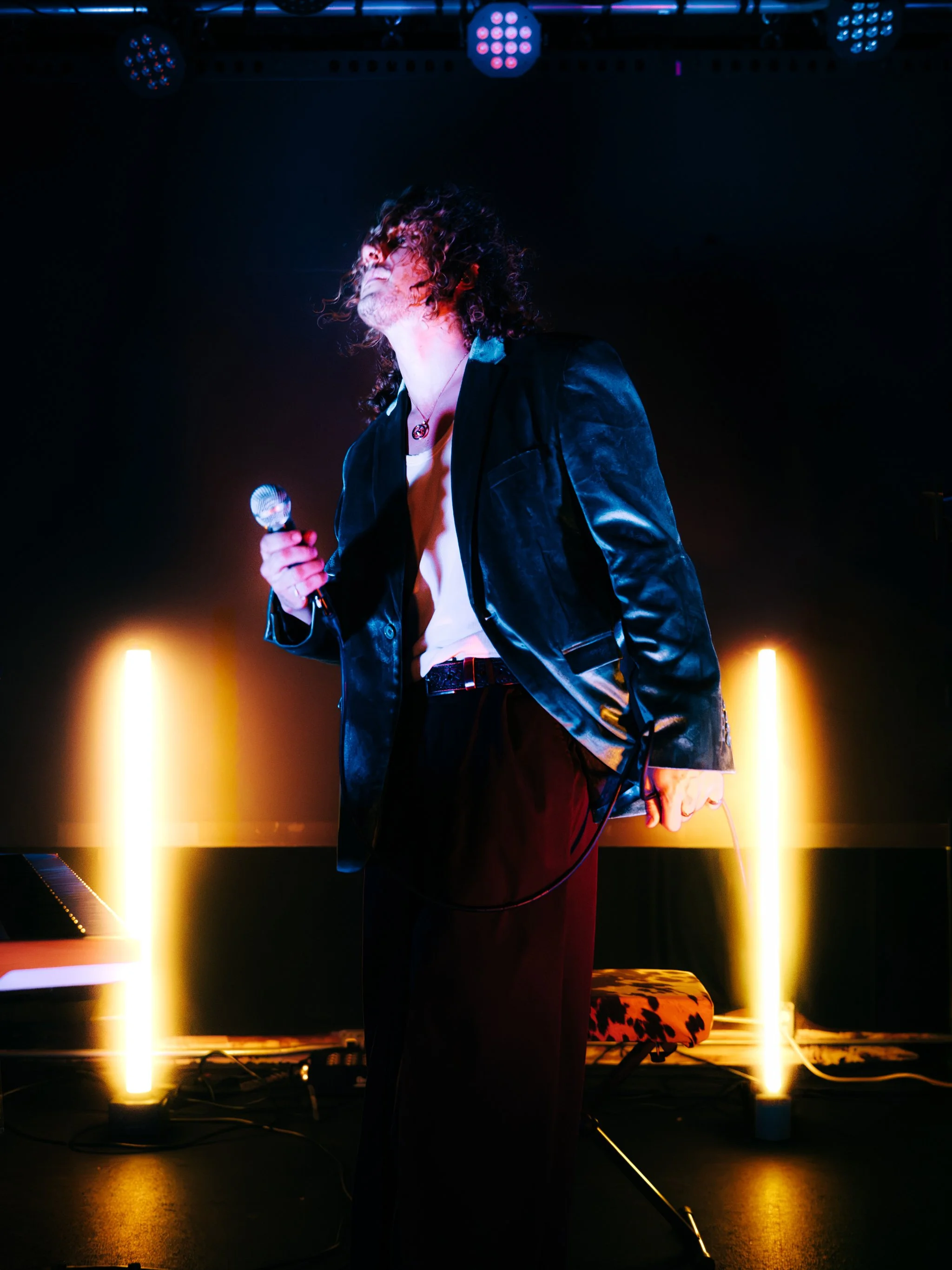 Singer in a velvet blazer holding a microphone between two glowing light tubes on stage