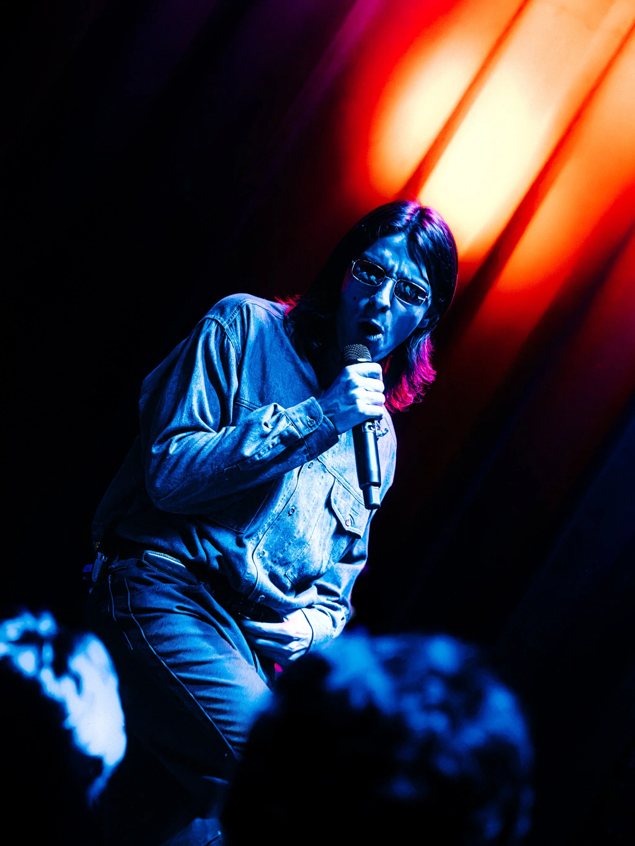 Singer in a denim jacket and sunglasses lit in blue with orange light streaks behind him